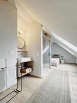 Quarto de loft moderno com claraboia, closet espaçoso e banheiro com um espelho grande e luminária.