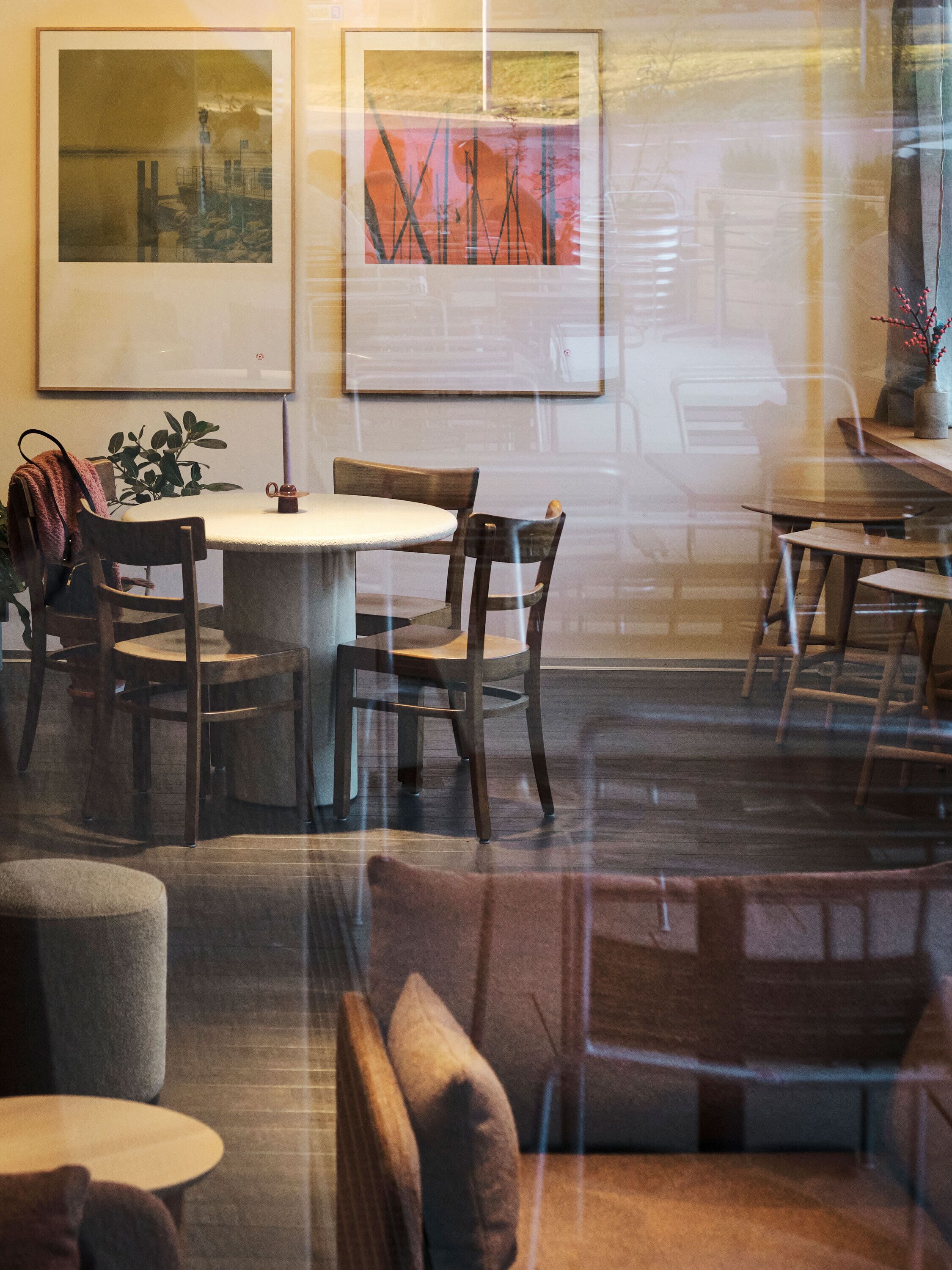 A dining area with round tables and chairs, a potted plant, and artwork on the walls.