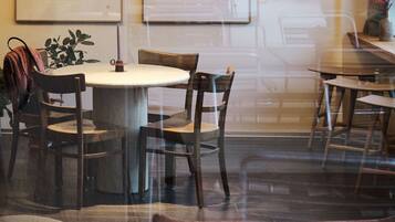 A dining area with round tables and chairs, a potted plant, and artwork on the walls.