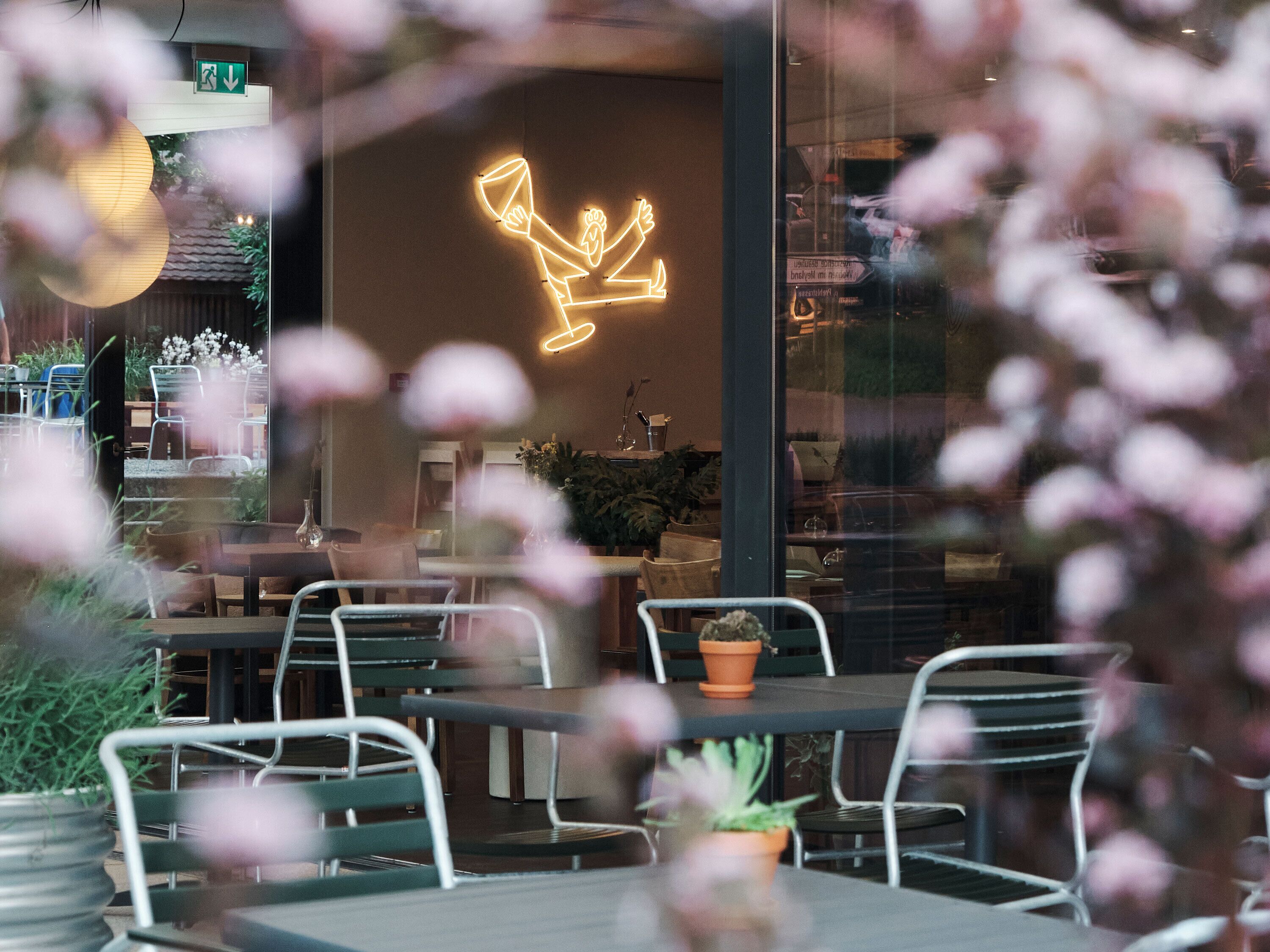 Un restaurante con mesas dentro, un letrero de neón y plantas en macetas.