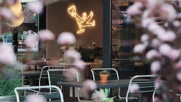 Un restaurante con mesas dentro, un letrero de neón y plantas en macetas.