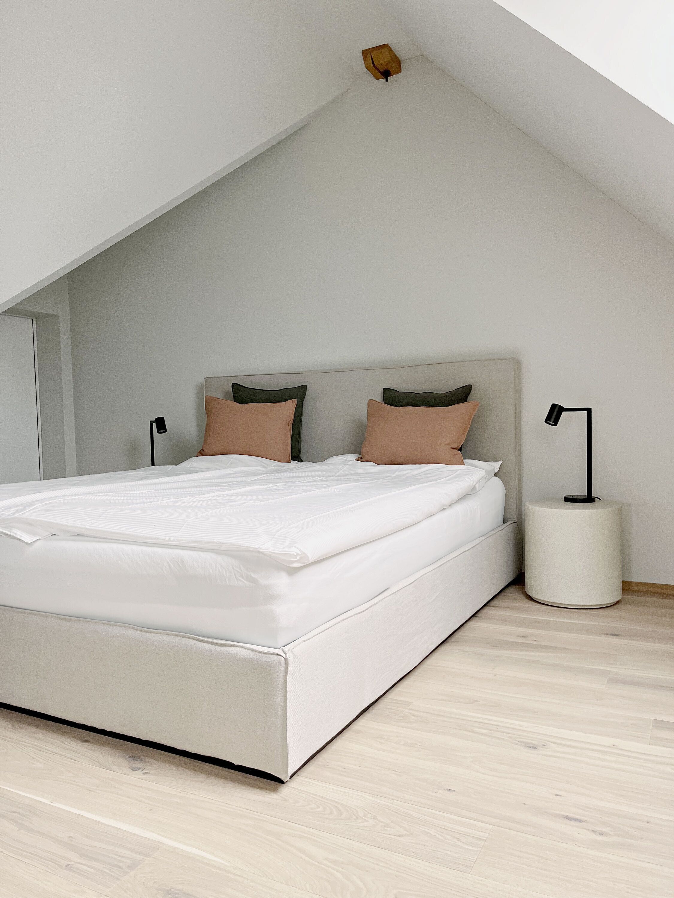 A modern bedroom with a sloped ceiling, a large bed, two bedside lamps, and a small bedside table.
