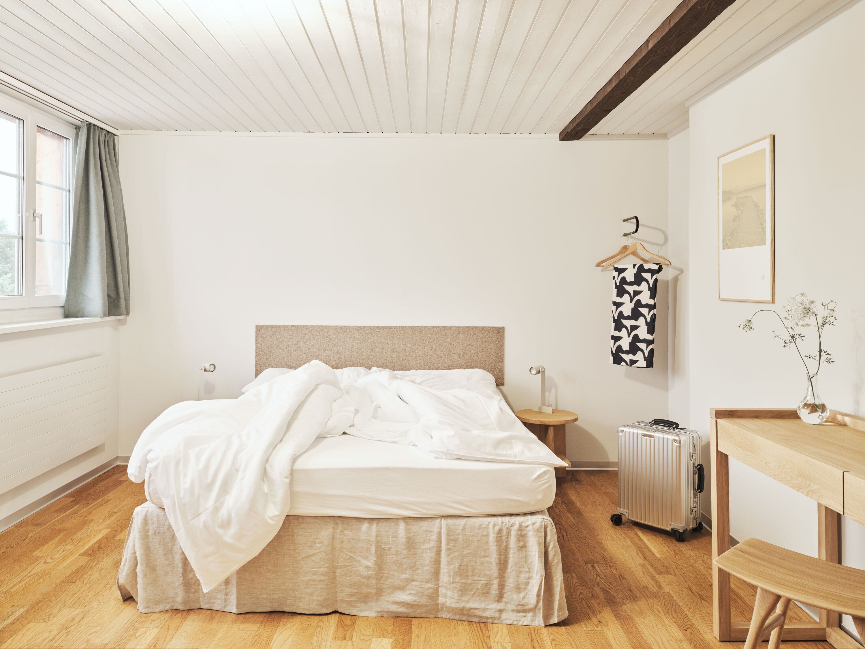 A bedroom with a bed, a wooden desk, a radiator, and a suitcase.