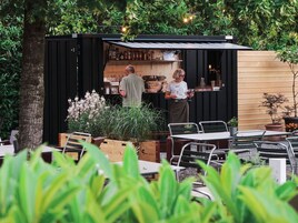 An outdoor bar area with a wooden counter, seating, and potted plants.