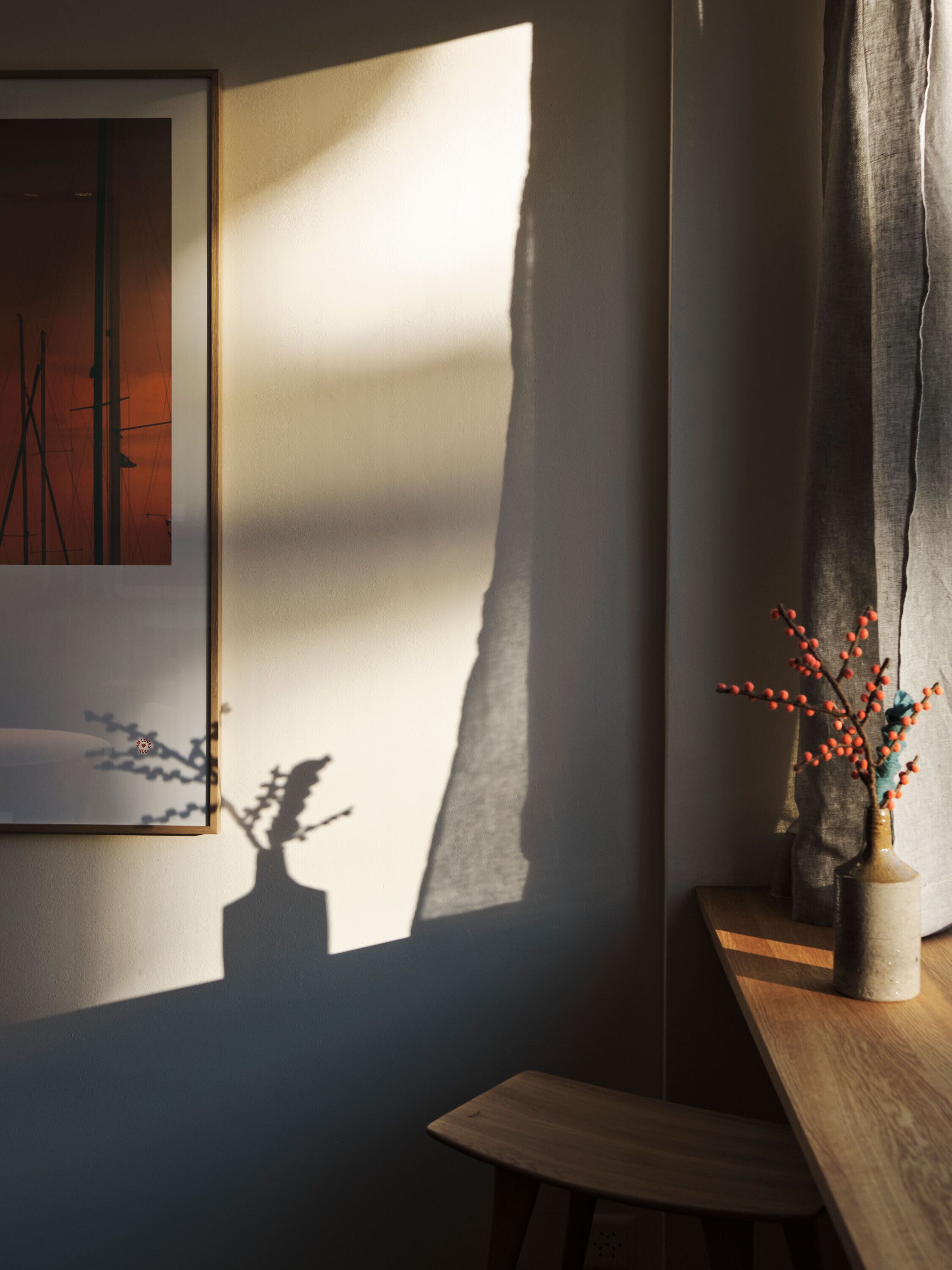 Una habitación con una obra de arte enmarcada en la pared, una mesa de madera y un jarrón con bayas rojas.
