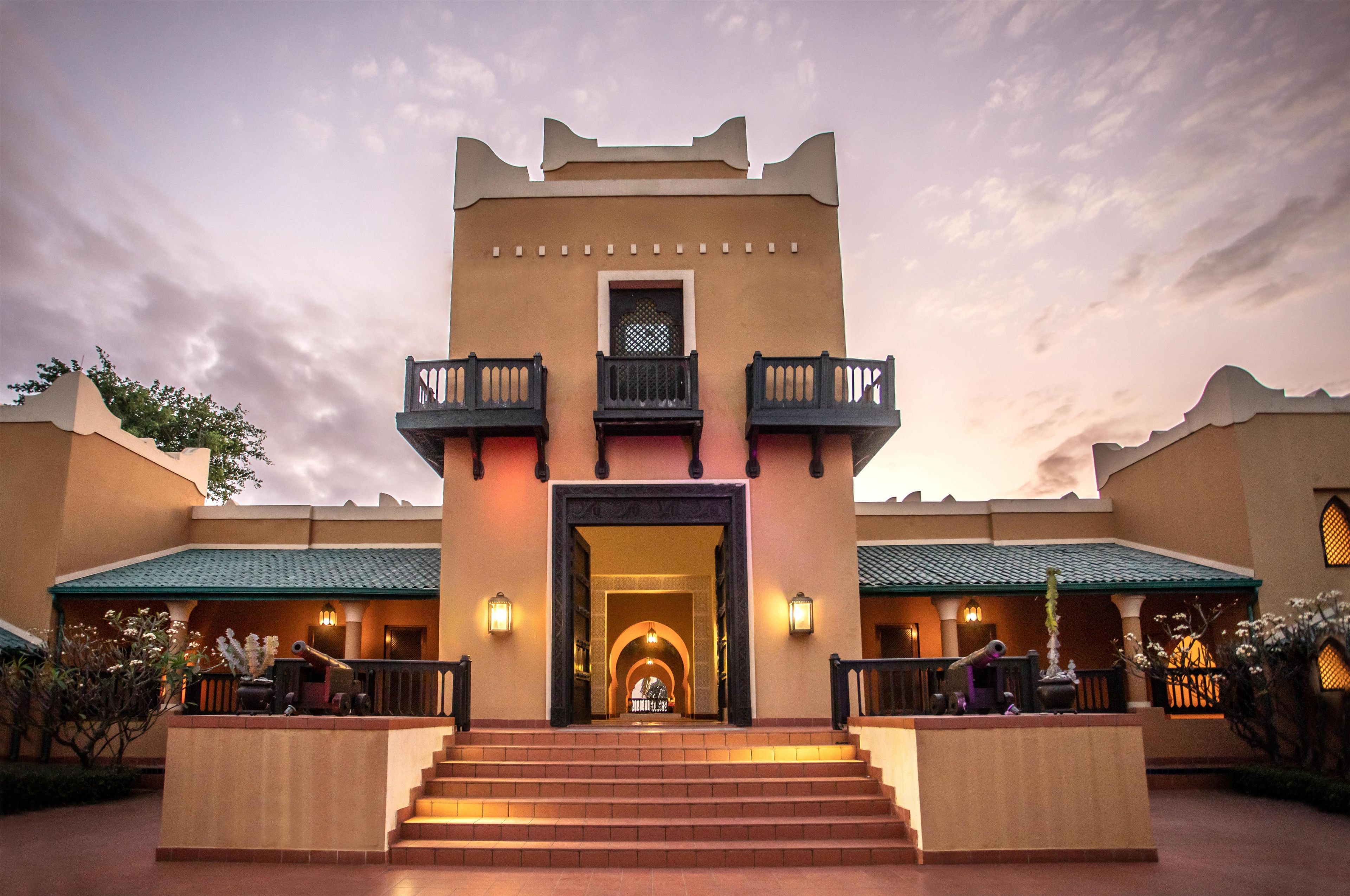 Entrada de hotel con un arco central, dos balcones a cada lado y una escalera que conduce a la entrada.