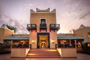 A hotel entrance with a central archway, two balconies on either side, and a staircase leading up to the entrance.
