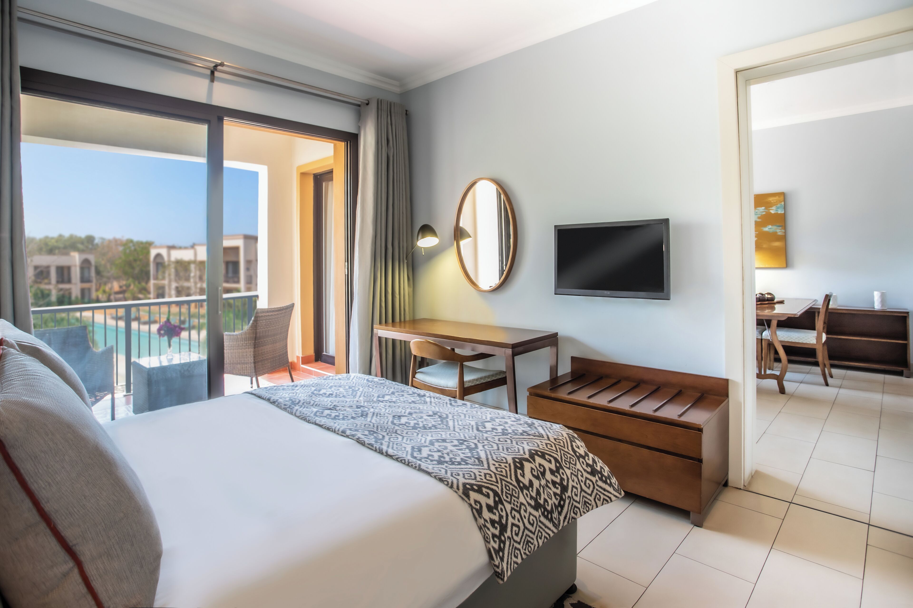 Habitación de hotel con cama, escritorio, silla, televisor y balcón con vista a la piscina.