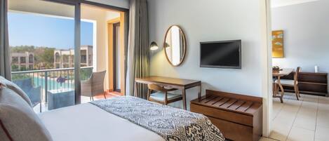 Habitación de hotel con cama, escritorio, silla, televisor y balcón con vista a la piscina.