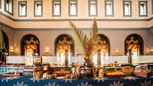 Un buffet proposant une variété de plats, agrémenté d’un élément décoratif central, dans une pièce dotée de fenêtres en arc de cercle et de murs à motifs.