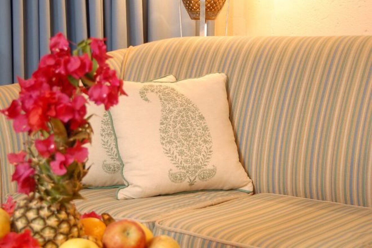 Un sofá a rayas con almohadones decorativos y una piña con fruta sobre una mesa.