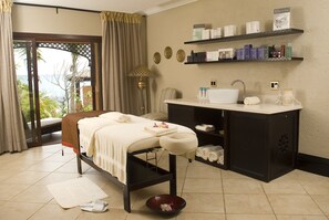 A spa room with a bed, a massage table, a sink, and shelves with toiletries. - Avani Pemba Beach Hotel (Pemba)