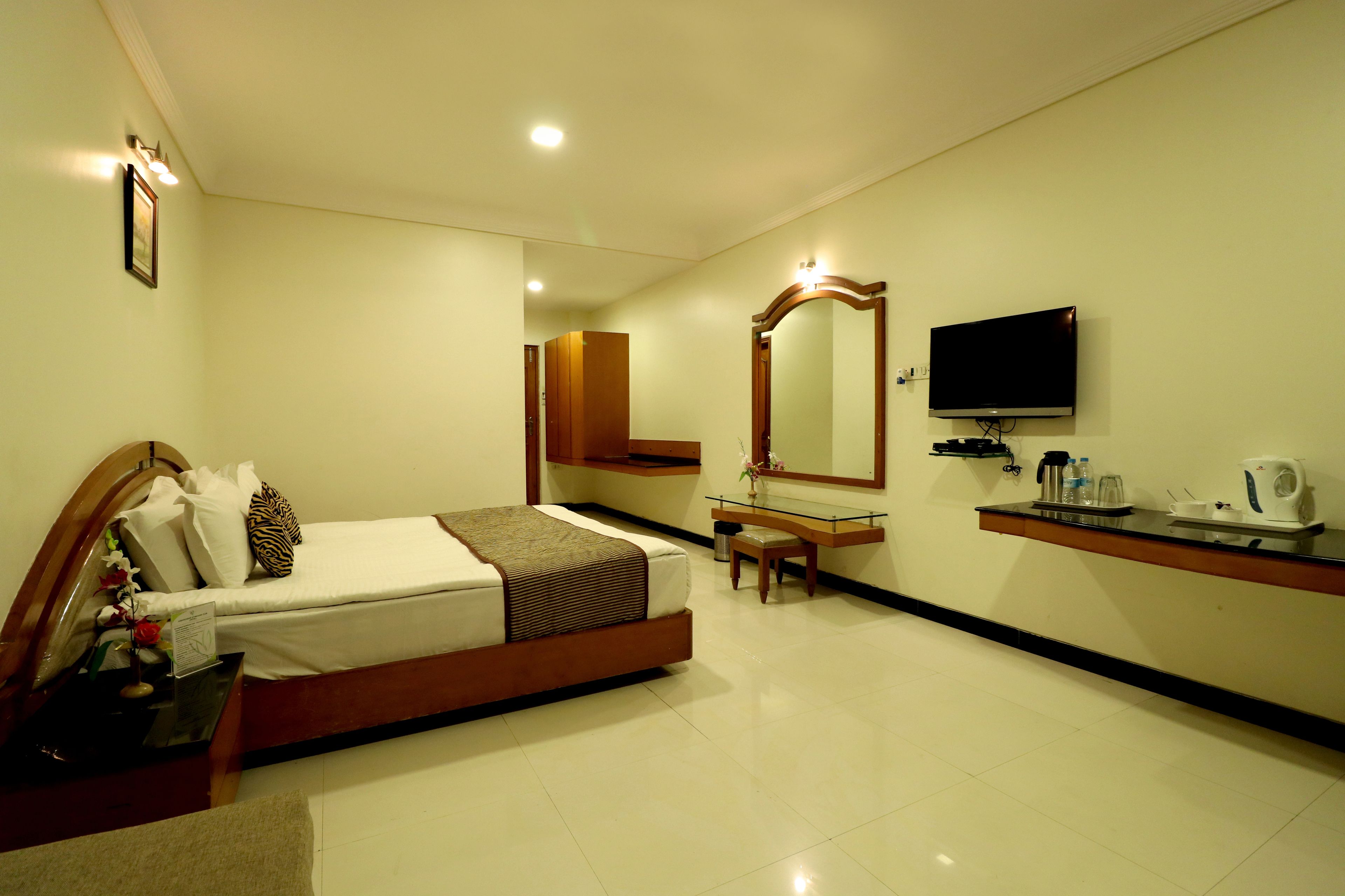 A hotel room with a bed, a desk, a mirror, a television, and a coffee maker.