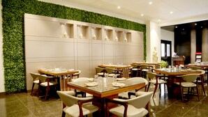 Un restaurante con varias mesas y sillas, una pared verde con plantas y una estatua en exhibición.