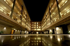 Un hotel a più piani con un atrio centrale, balconi su ogni piano e un pavimento lucido e riflettente.
