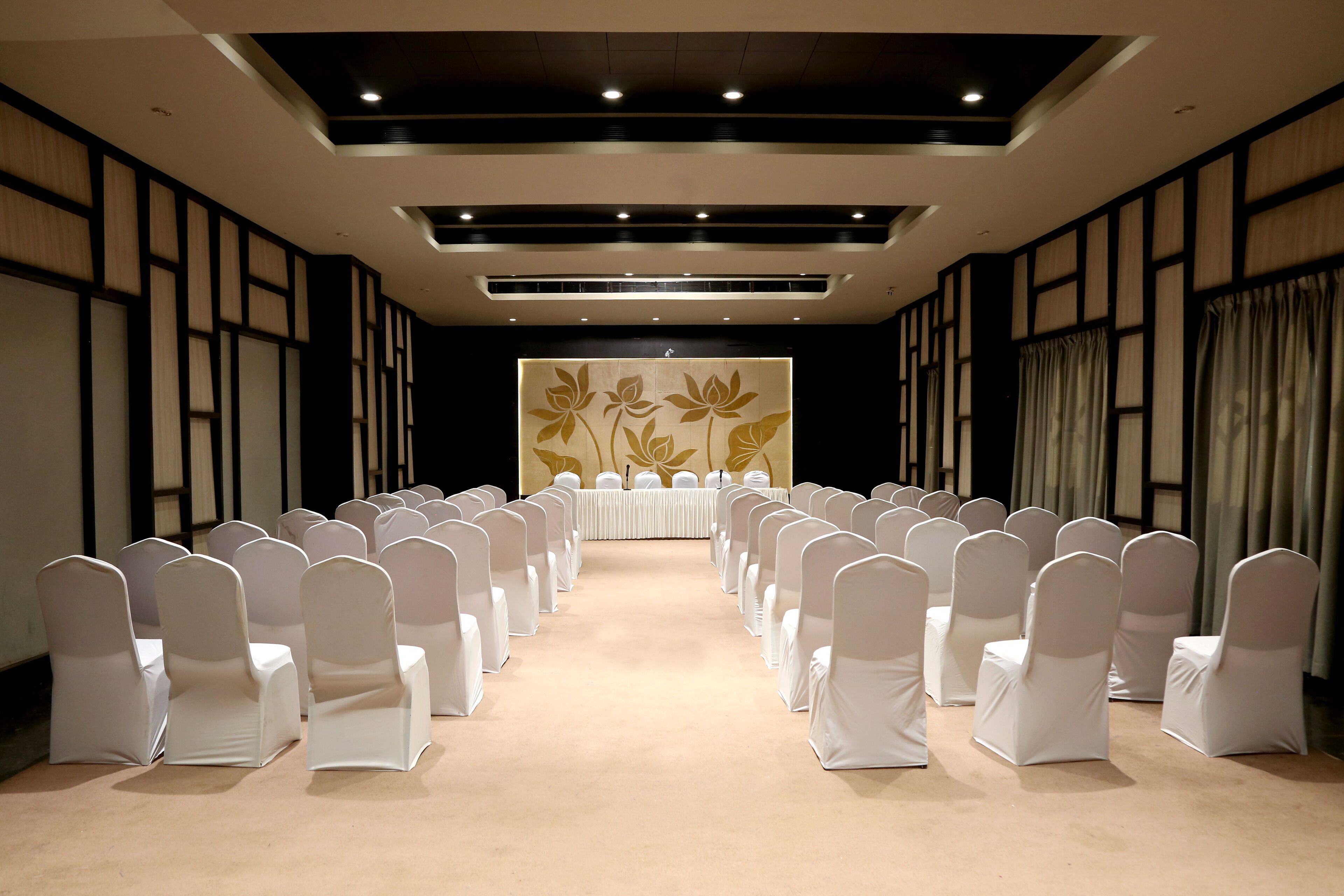 A conference room with rows of white chairs, a long table, and a floral wall decoration.