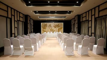 A conference room with rows of white chairs, a long table, and a floral wall decoration.