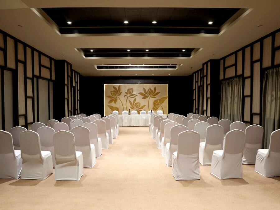 A conference room with rows of white chairs, a long table, and a floral wall decoration.