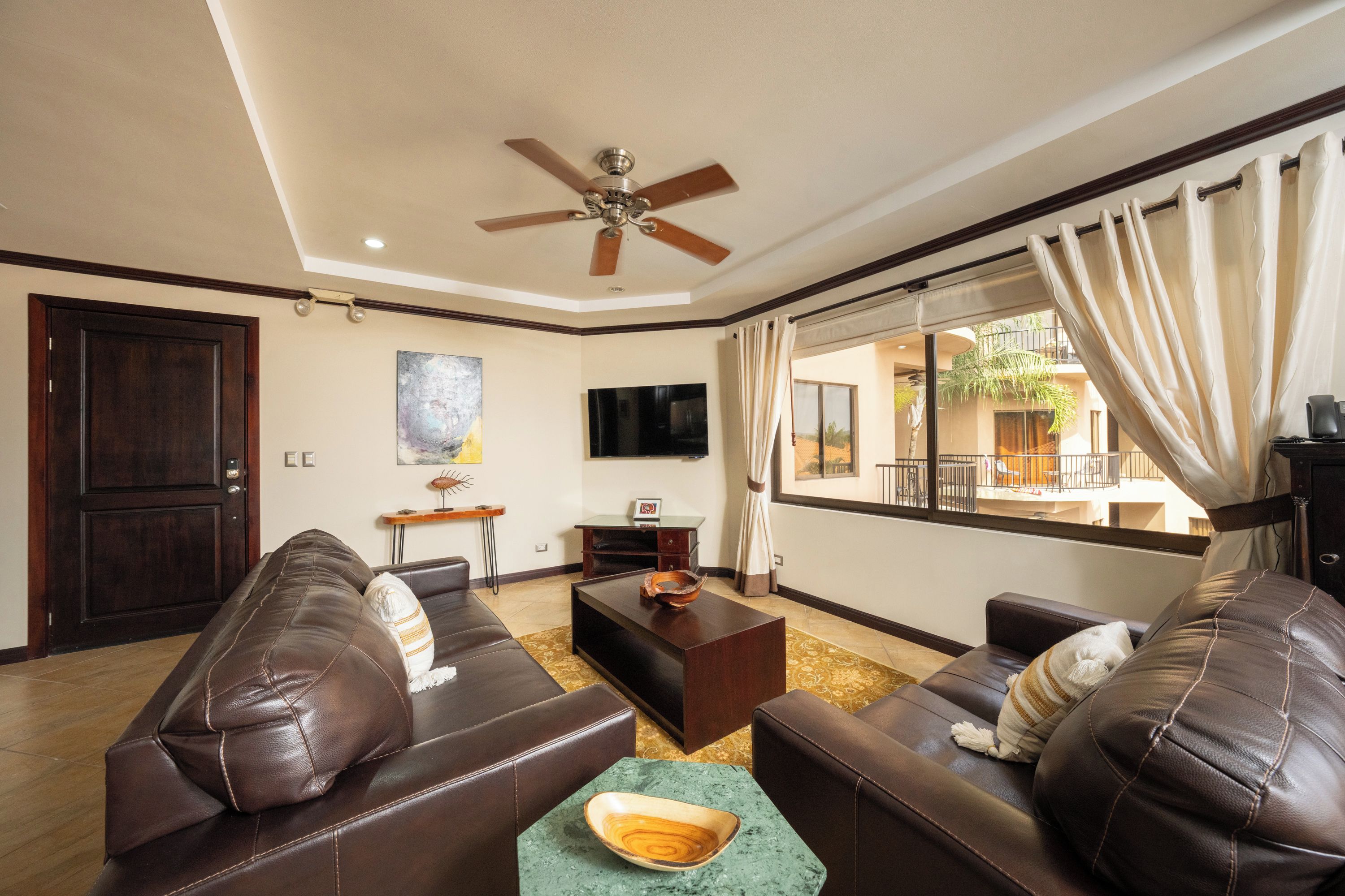 A living room with leather sofas, a coffee table, a flat-screen TV, and a ceiling fan.