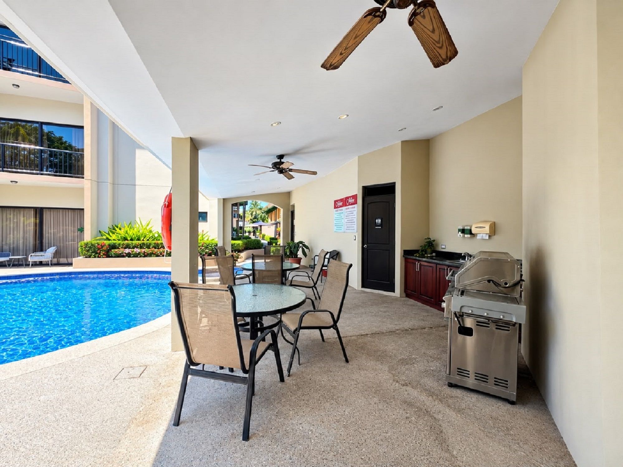 A poolside area with a table and chairs, a ceiling fan, and a barbecue grill.