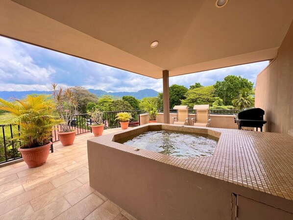 Terraza en la azotea con jacuzzi, plantas en macetas y una parrilla.