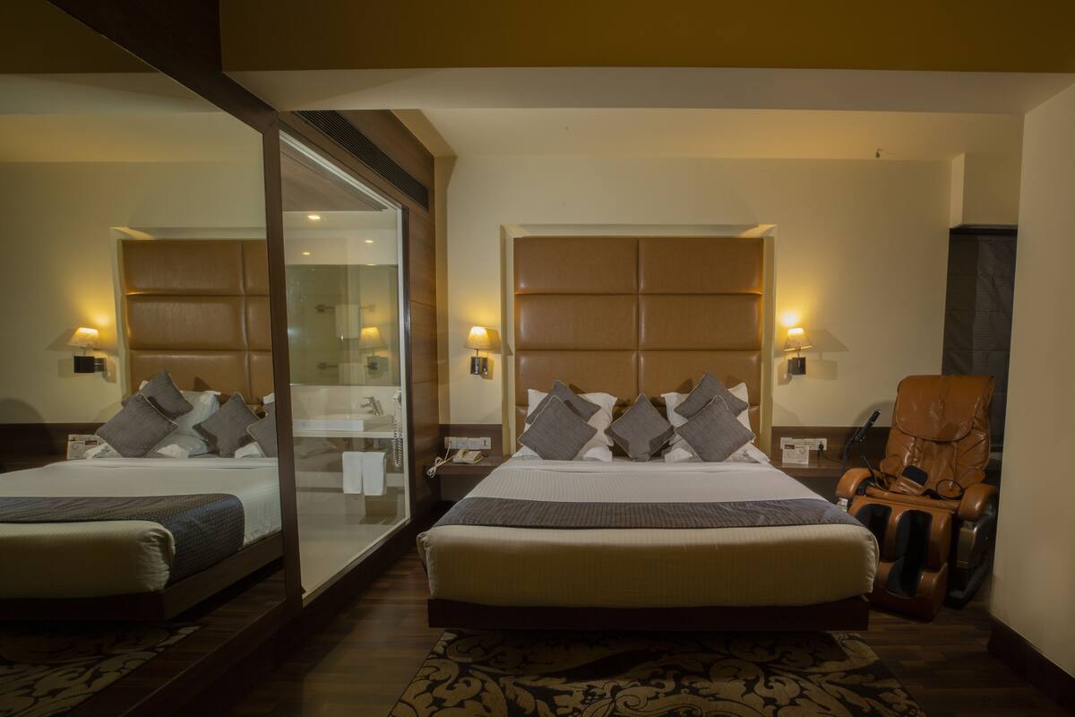 A hotel room with a large bed, a massage chair, a glass shower enclosure, and a nightstand with a lamp.