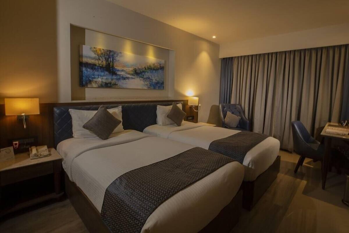 A hotel room with two beds, a desk, a chair, and a large painting on the wall.