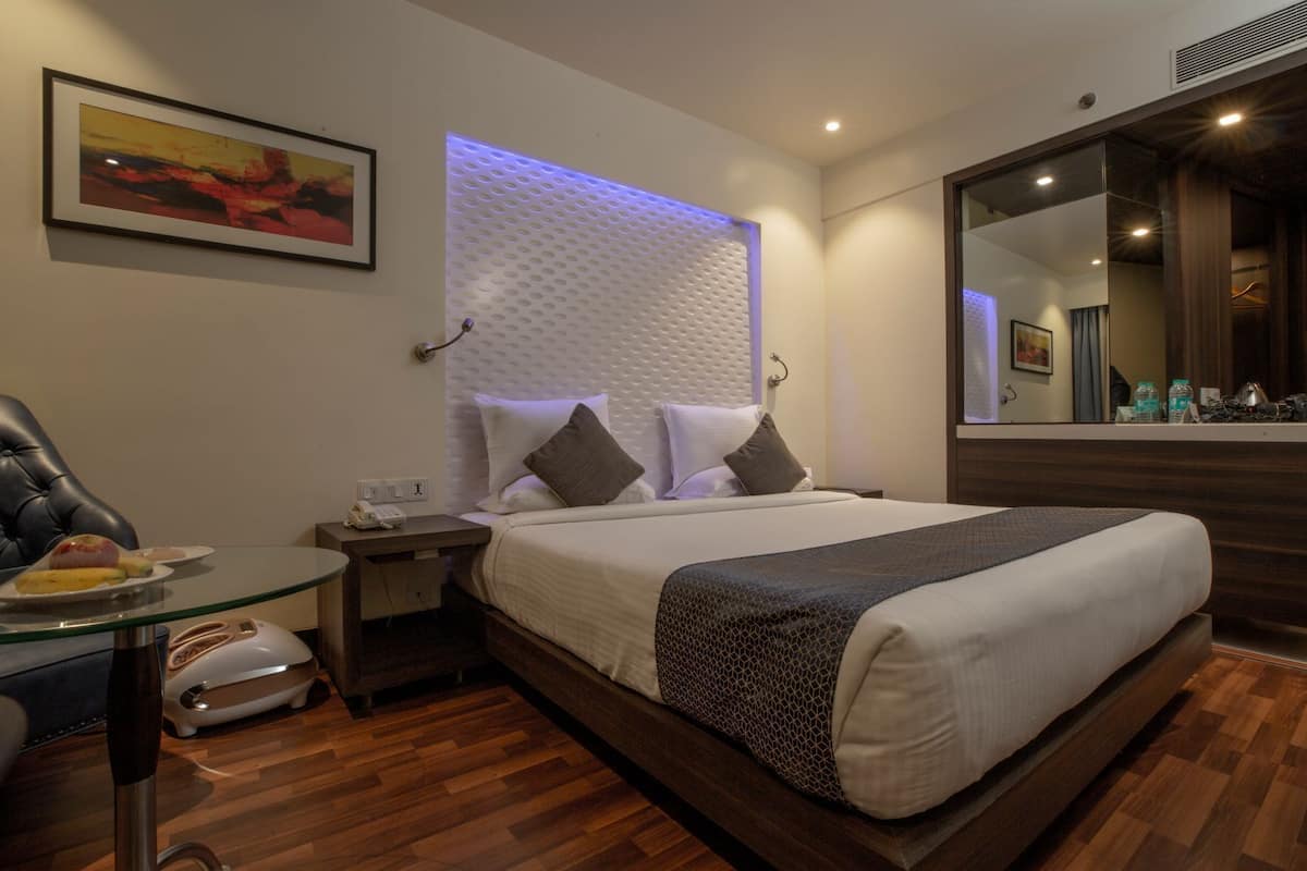 A hotel room with a bed, bedside table, and a mirror.