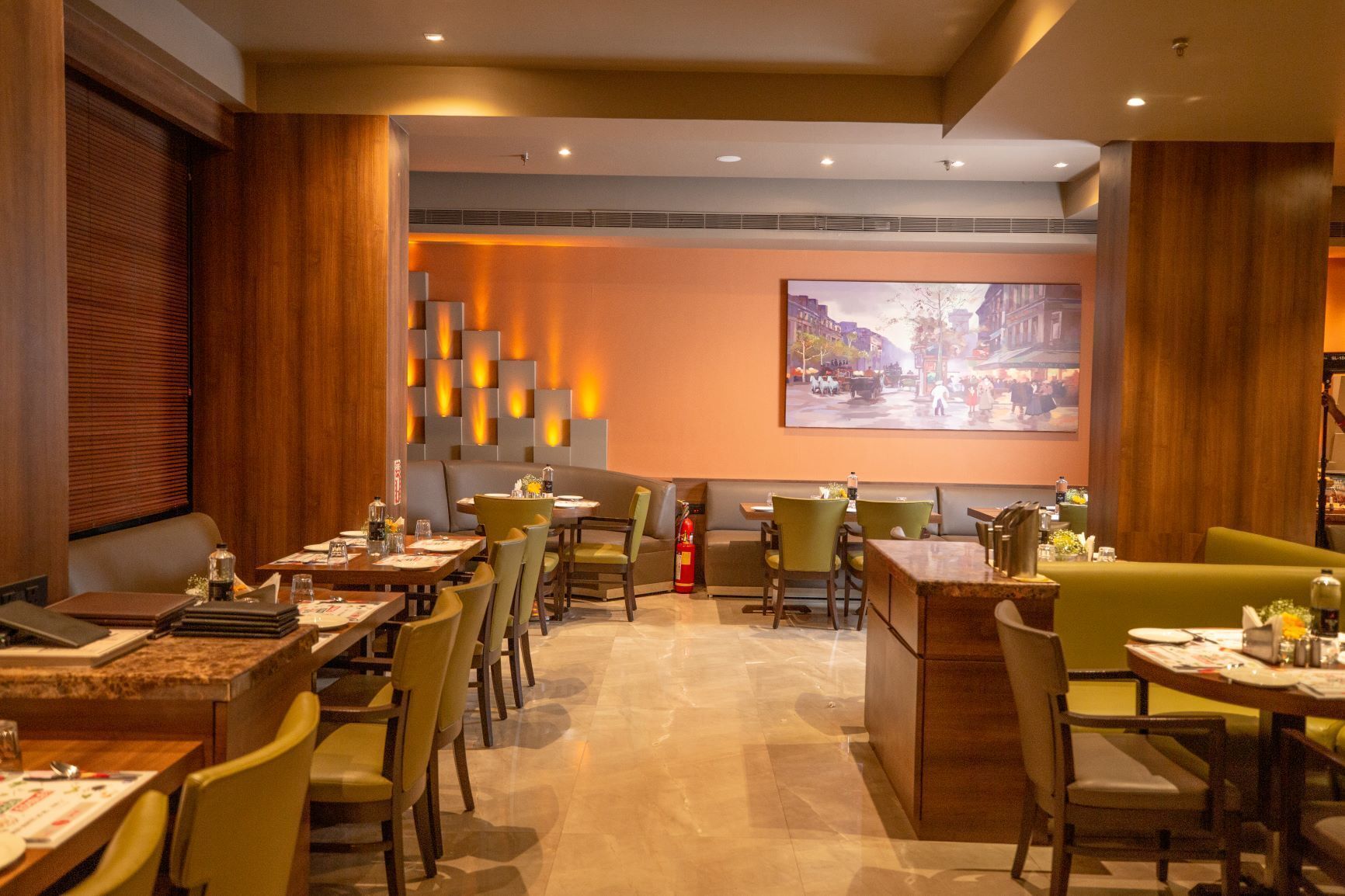 A restaurant with booths and tables, a fire extinguisher, and a cityscape painting on the wall.