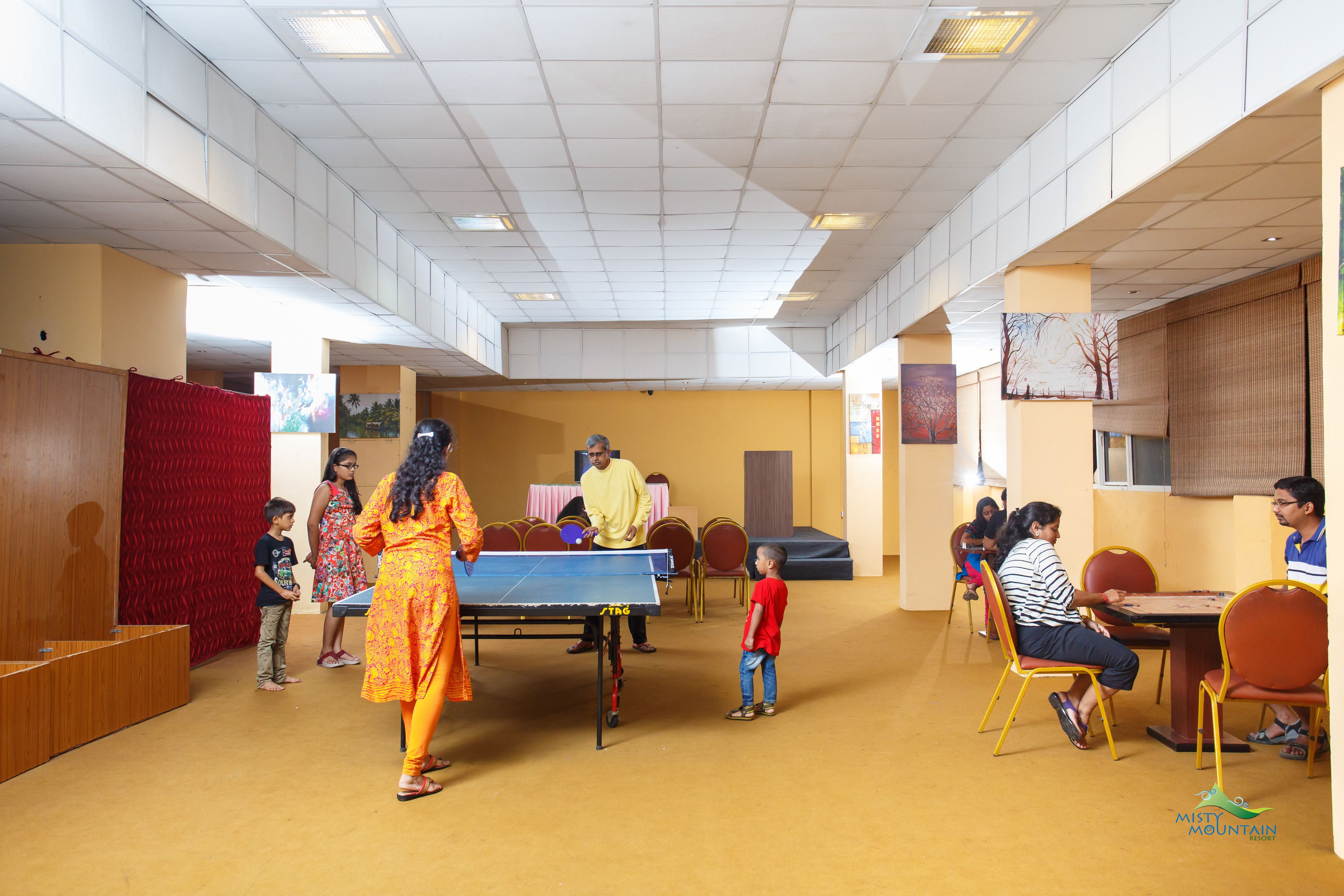 Amplio espacio interior con mesa de ping pong, sillas y un escenario con fondo.