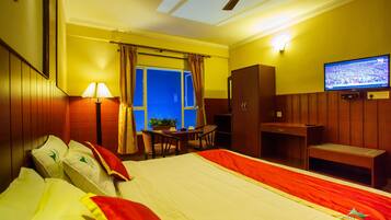 Ein Hotelzimmer mit Bett, Schreibtisch, Stuhl, Fernseher und einem Fenster mit Vorhängen.