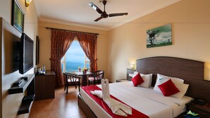 Habitación de hotel con cama, escritorio, televisor, ventana con cortinas y un cuadro en la pared.