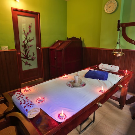 A room with a wooden bed, a small table with candles, a clock on the wall, and a wooden cabinet.