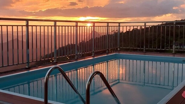 Una piscina con barandilla metálica, con vistas a montañas y al atardecer.