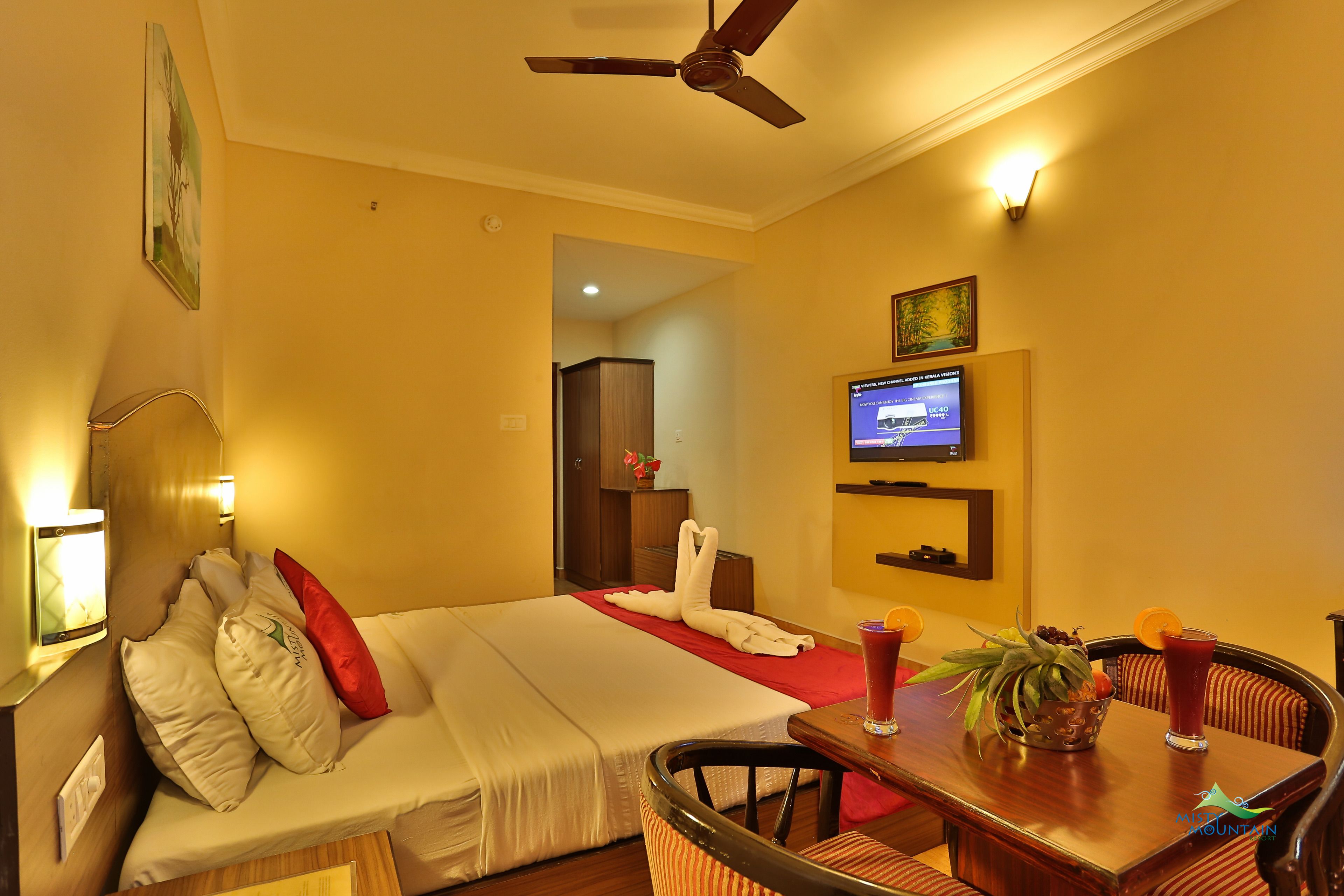 Una habitación de hotel con cama, televisor, mesa de comedor con sillas y ventilador de techo.