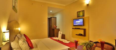 Una habitación de hotel con cama, televisor, mesa de comedor con sillas y ventilador de techo.
