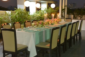 An outdoor dining area with a table set for six, surrounded by chairs, and decorated with candles and flowers. - Rockland Hotel - C R Park (New Delhi)