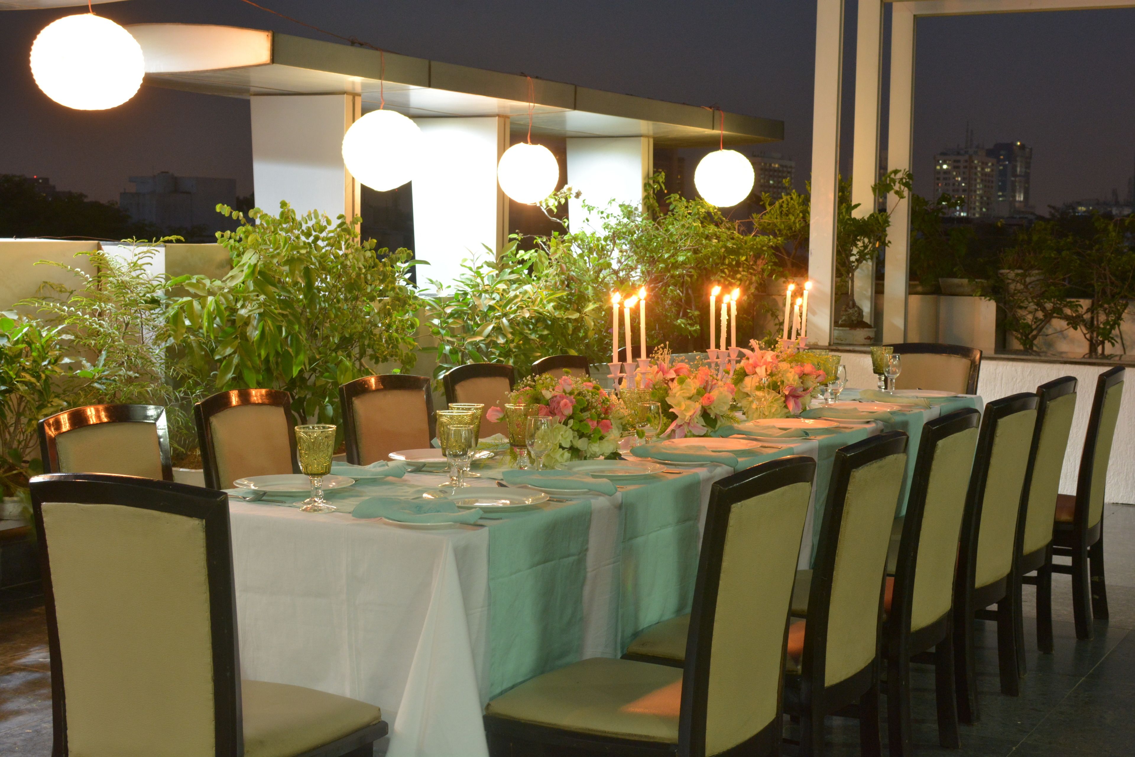 An outdoor dining area with a table set for six, surrounded by chairs, and decorated with candles and flowers.