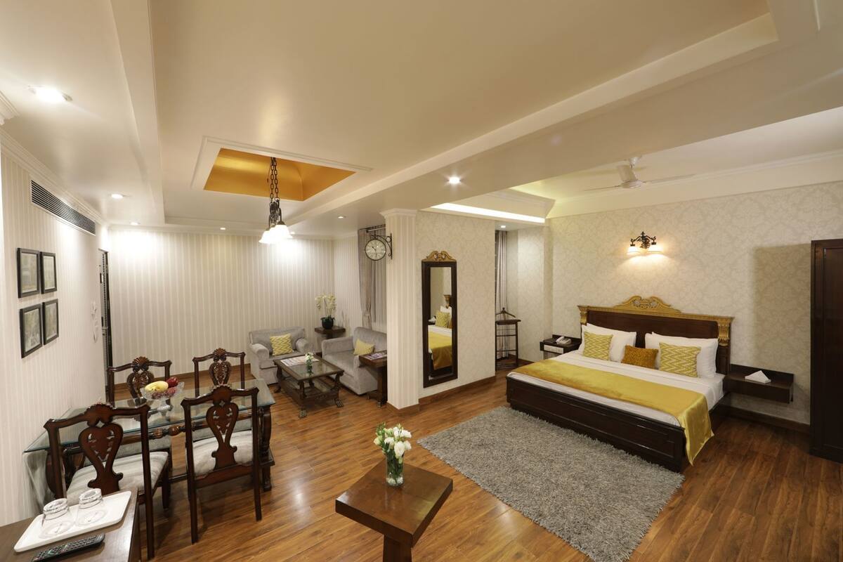 A hotel room with a bed, a desk, a chair, a sofa, a dining table, and a mirror.