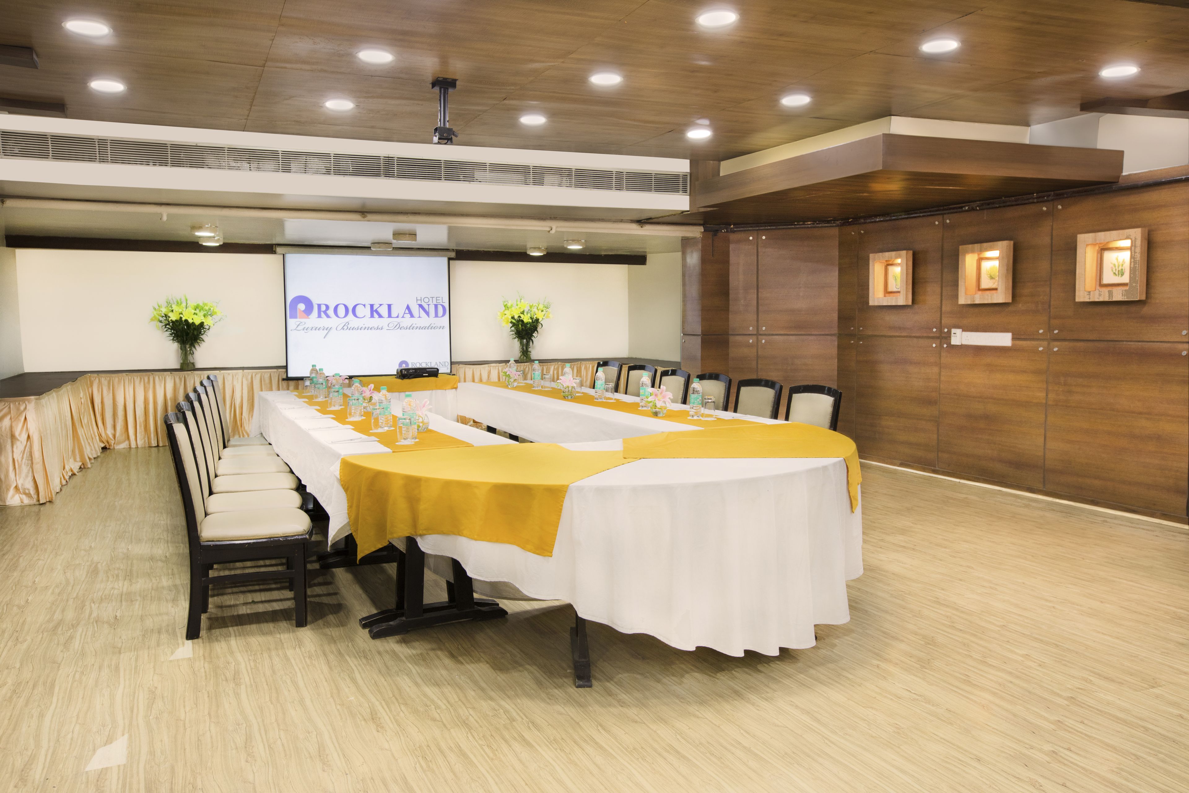 Un salón de conferencias con una larga mesa, sillas y una pantalla de proyector que muestra 