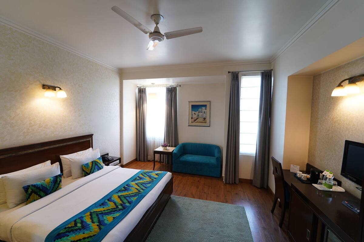 A hotel room with a bed, a desk, a chair, a television, and a ceiling fan.