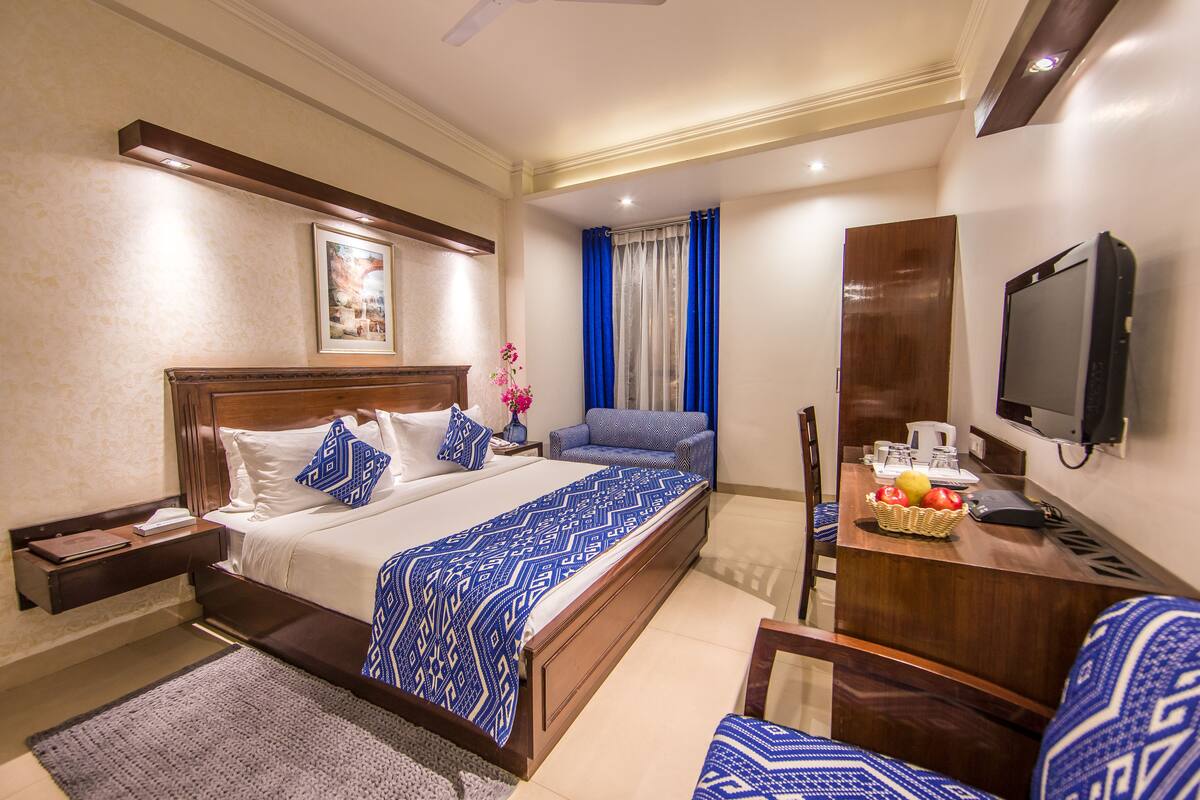 A hotel room with a large bed, a desk with a chair, a television, and a window with blue curtains.
