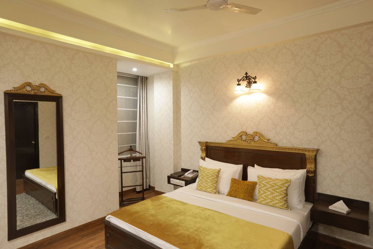 A hotel room with a large bed, a nightstand, a bedside table, a mirror, a wardrobe, and a ceiling fan.