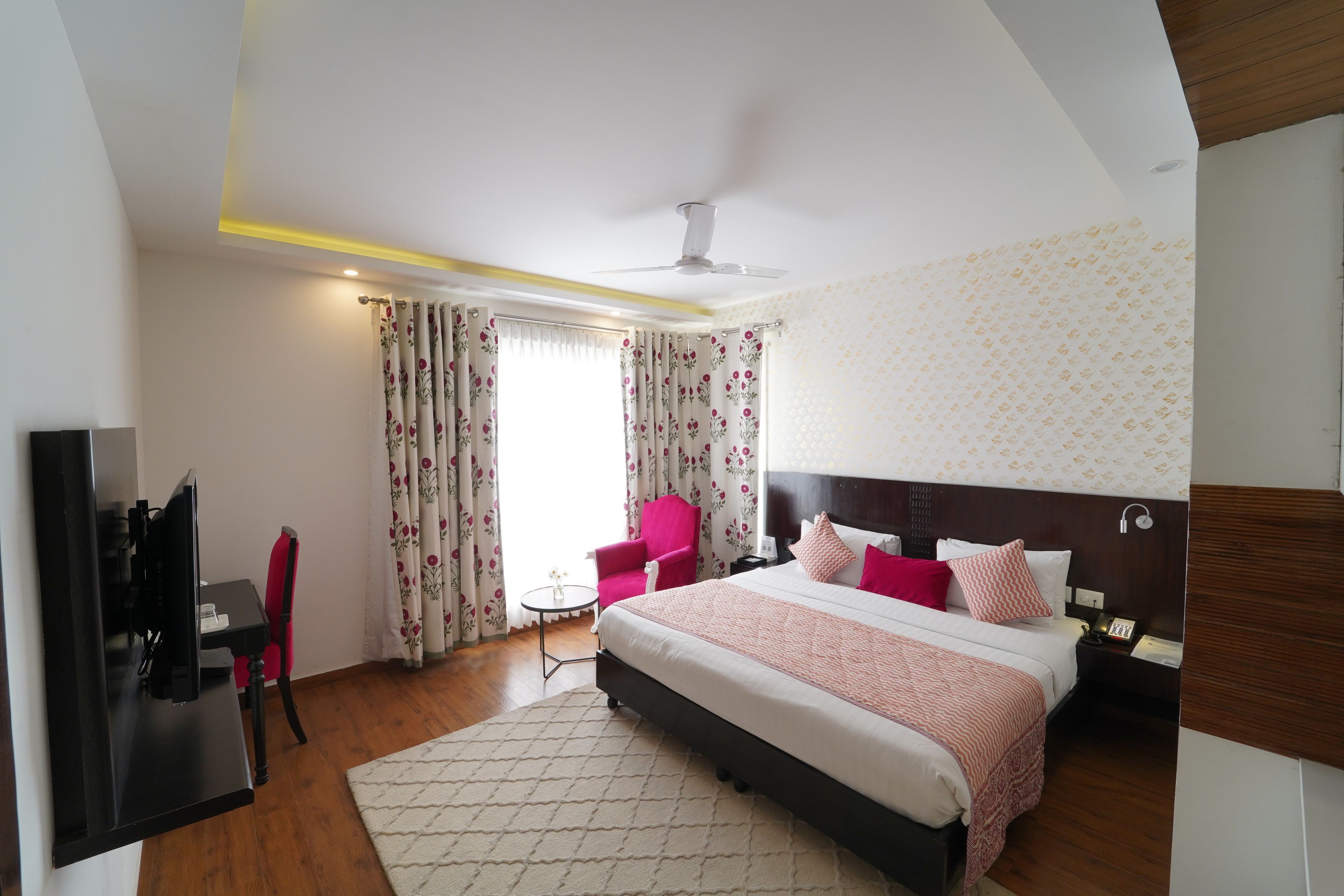 Una habitación de hotel con cama, escritorio, silla, televisión y ventilador de techo.