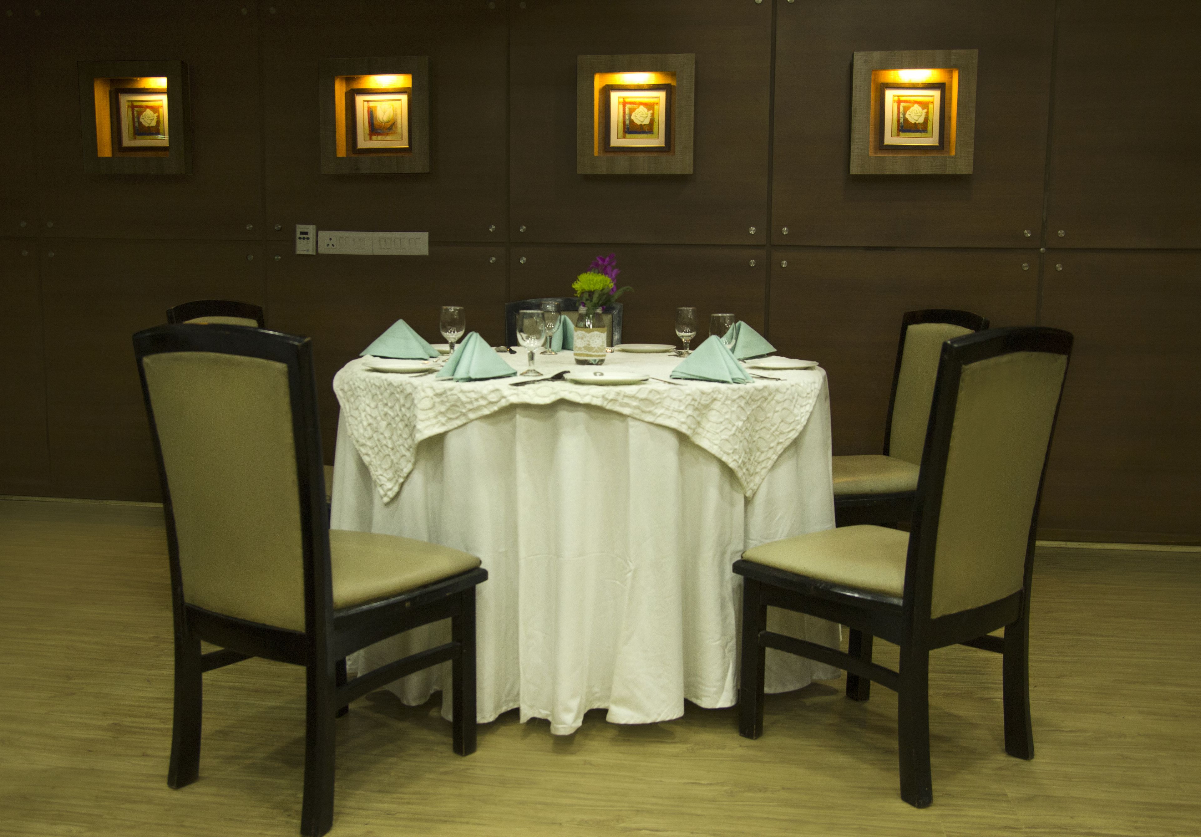 A dining table set for four with chairs, a white tablecloth, and a vase with flowers.