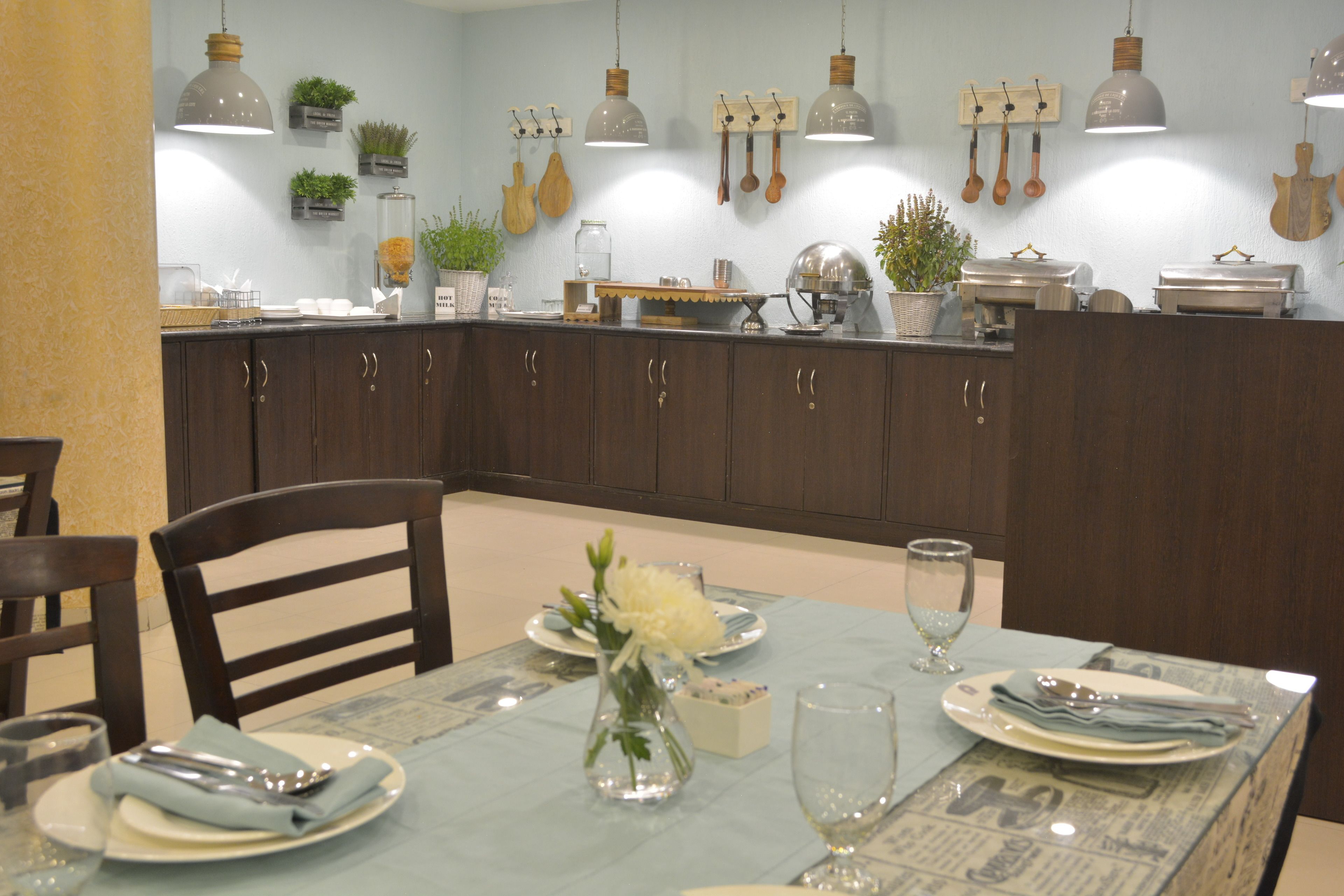 Un comedor con una mesa preparada para cuatro personas, adornada con un jarrón de flores, platos y cubiertos.