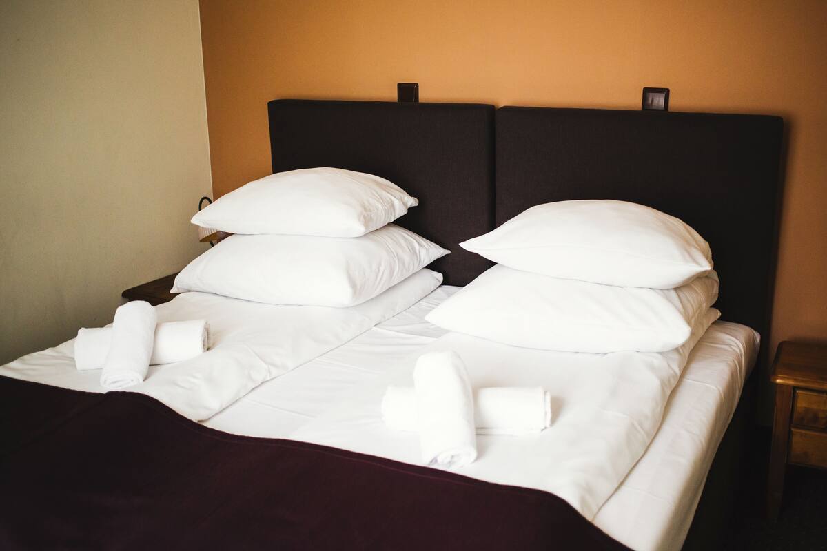 A neatly made bed with white linens and pillows, a dark headboard, and a small bedside table with a clock.
