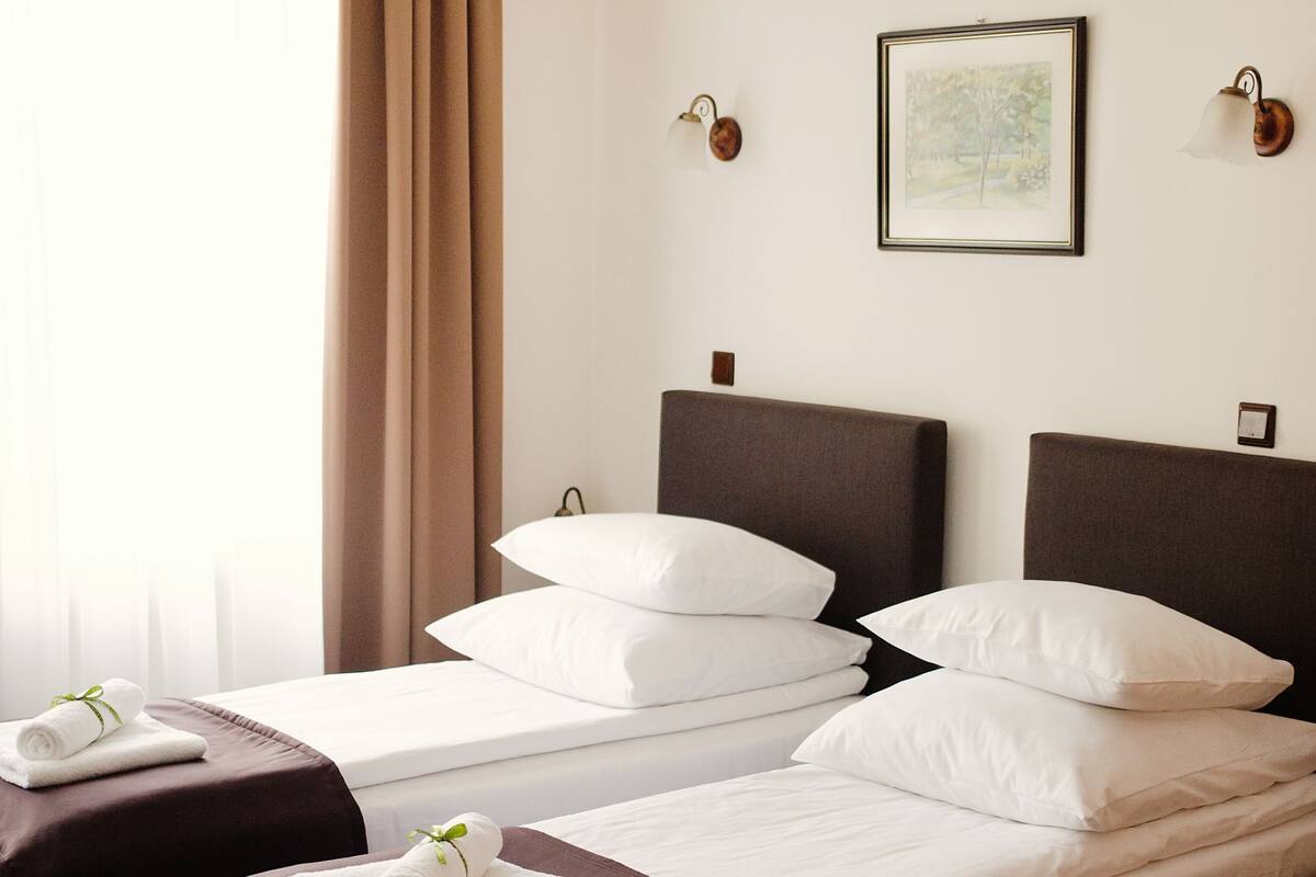 A hotel room with two beds, a chandelier, a framed picture on the wall, and a window with curtains.
