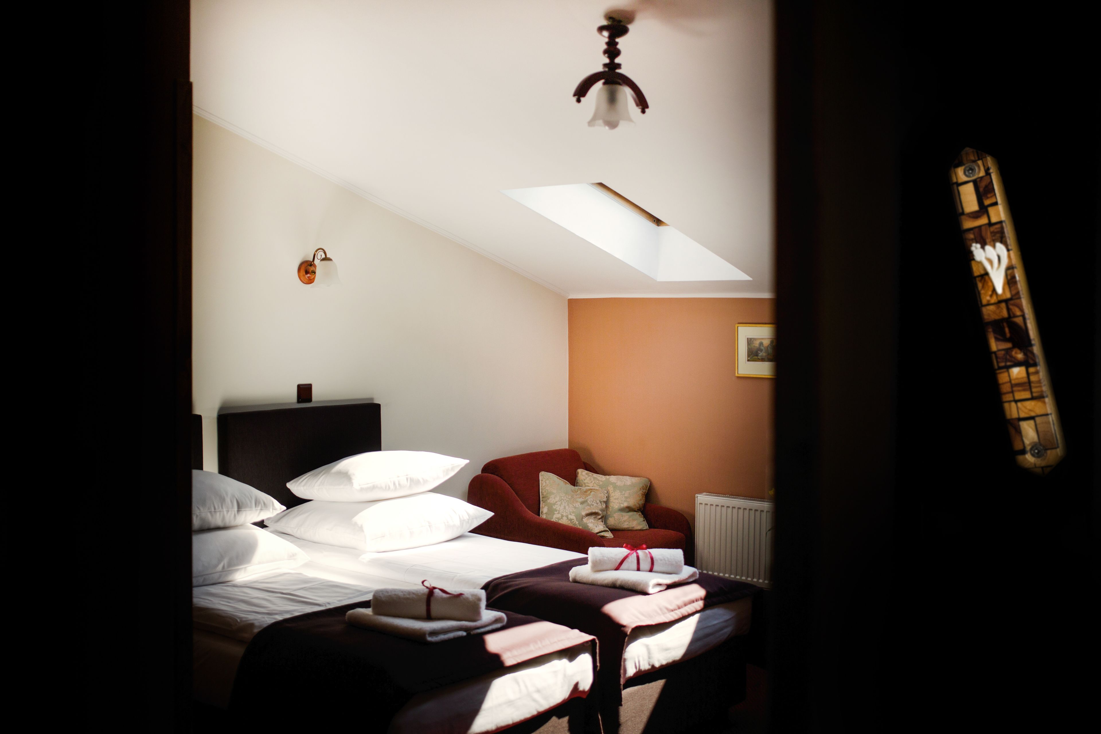 Un dormitorio con una cama, un sillón rojo, un radiador y un tragaluz.