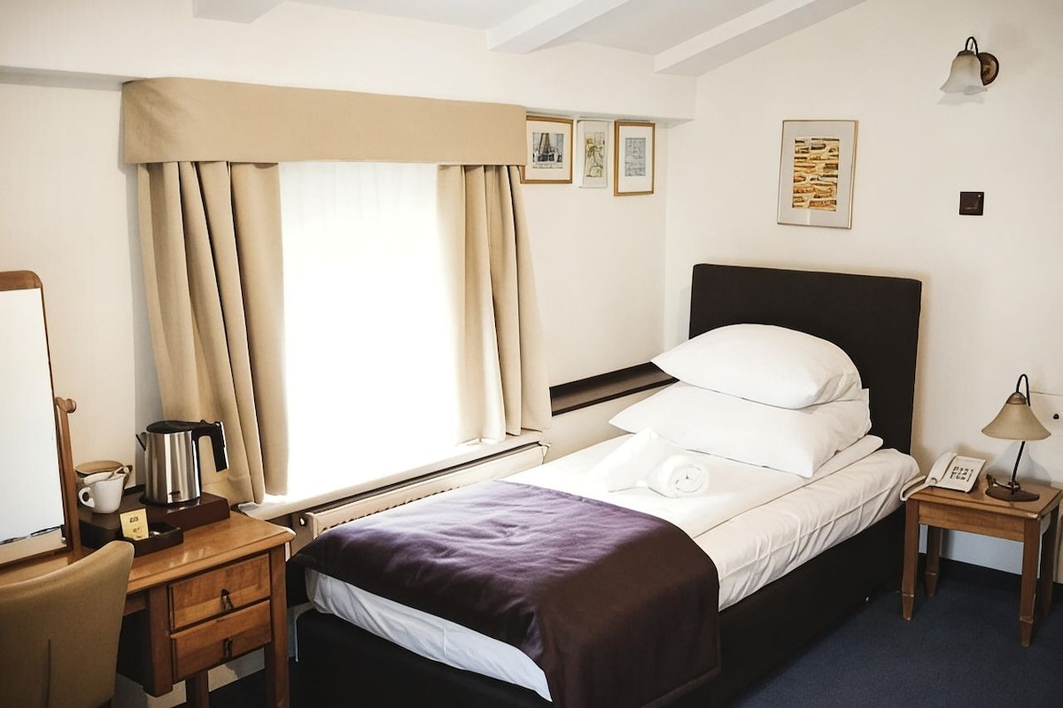 A hotel room with a bed, bedside table, lamp, and a window with curtains.